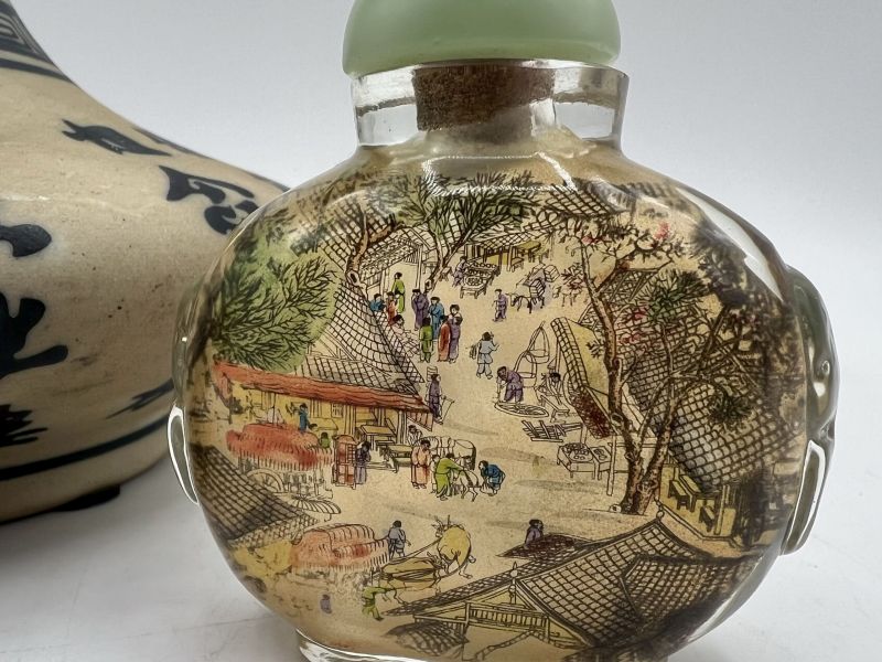 Antique Chinese 3-inch snuff bottle with inside-painted village scene, detailed figures, rooftops, and trees under glass with pale green stopper.