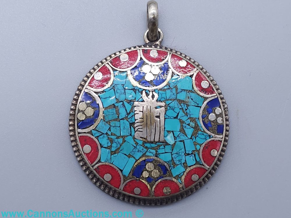 Tibetan or Nepalese silver pendant with turquoise, coral, and lapis mosaic inlay and central Tibetan protection symbol, approximately 1.75 inches in diameter.