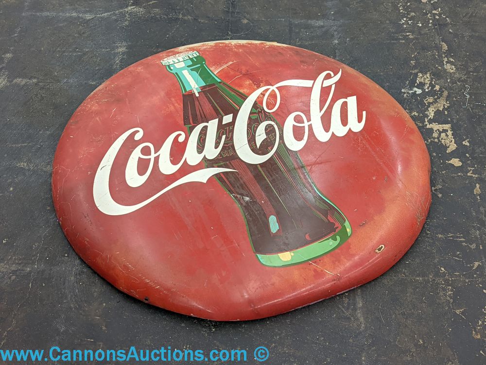 Vintage Coca-Cola round enameled metal button sign with red background, white “Coca-Cola” script, and bottle graphic