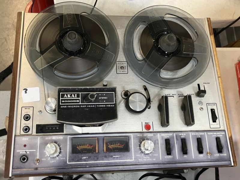 Top view of an Akai 4000DS reel-to-reel tape recorder with two clear take-up reels, brushed silver faceplate, dual VU meters, and transport controls.