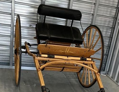 Meadowbrook wooden horse-drawn carriage with black leather seats, spoked wheels, and decorative trim shown in storage unit setting