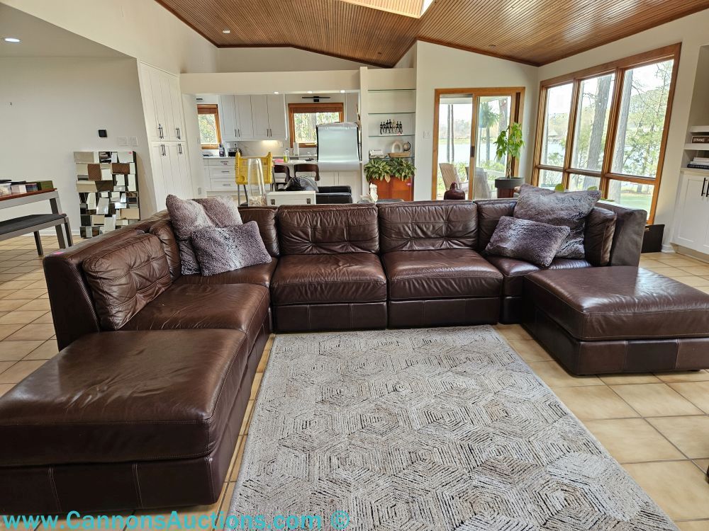 Seven-piece brown leather sectional sofa with plush accent pillows in a contemporary living room with tile flooring, large windows, and open kitchen beyond; each section measures 36" x 36" x 31".