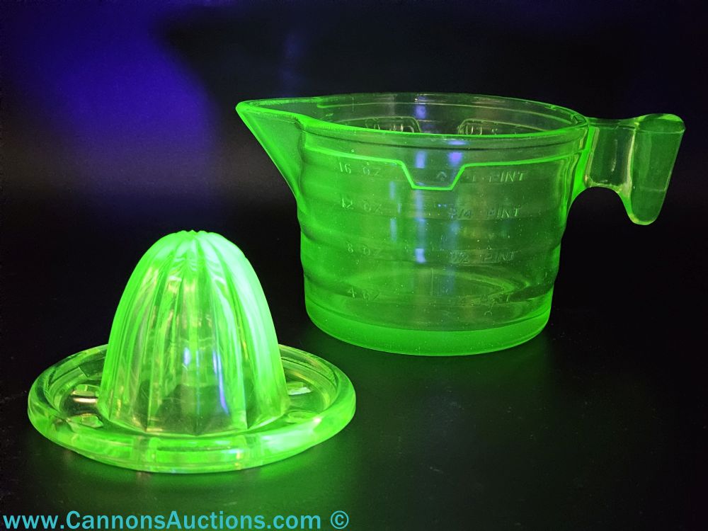 Vintage uranium glass citrus juicer with reamer and measuring cup marked in ounces and pints, shown glowing bright green under UV light.