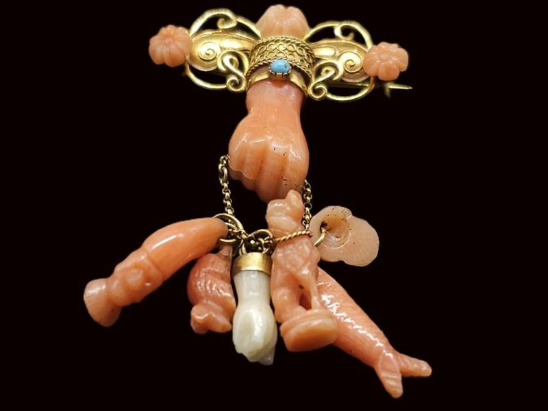 Antique Italian-style coral mano figa charm brooch with gold-tone filigree bar, carved coral fist amulet, dangling coral charms, and blue accent stone