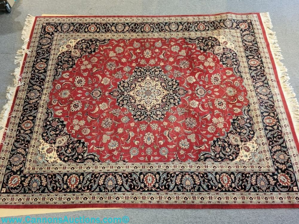 Hand-knotted Pakistani wool rug with red field, black floral border, central medallion, and fringe, 96 x 130 inches