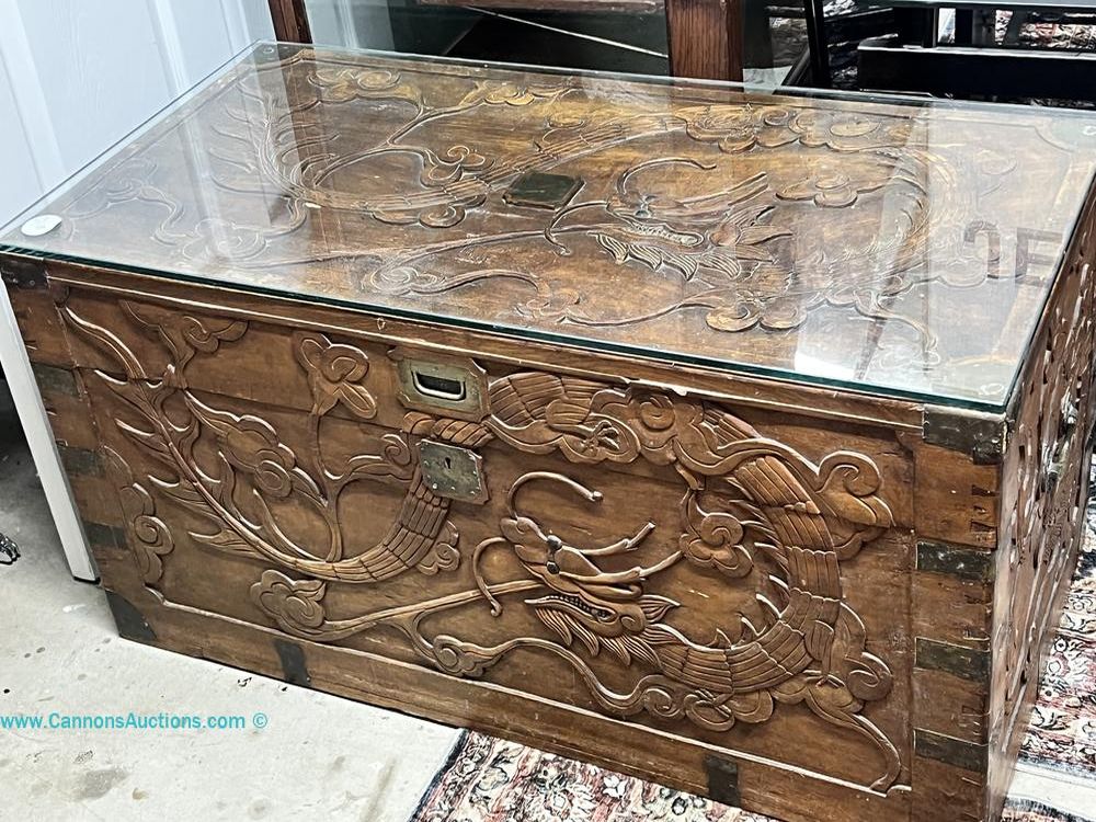 Chinese camphor-wood chest with carved dragon and floral motifs, fitted glass top, hinged lid, and interior storage.