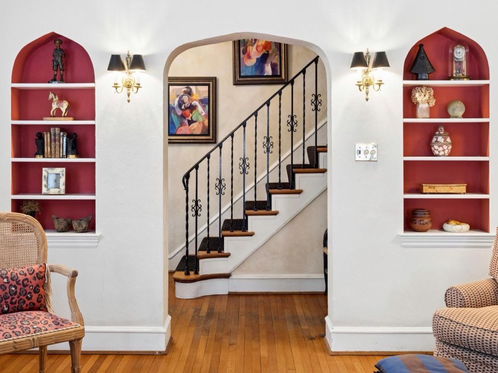 Interior of a Kingcrest Parkway Richmond estate featuring an arched staircase, built-in red display shelves, artwork, decorative objects, wall sconces, and upholstered seating.