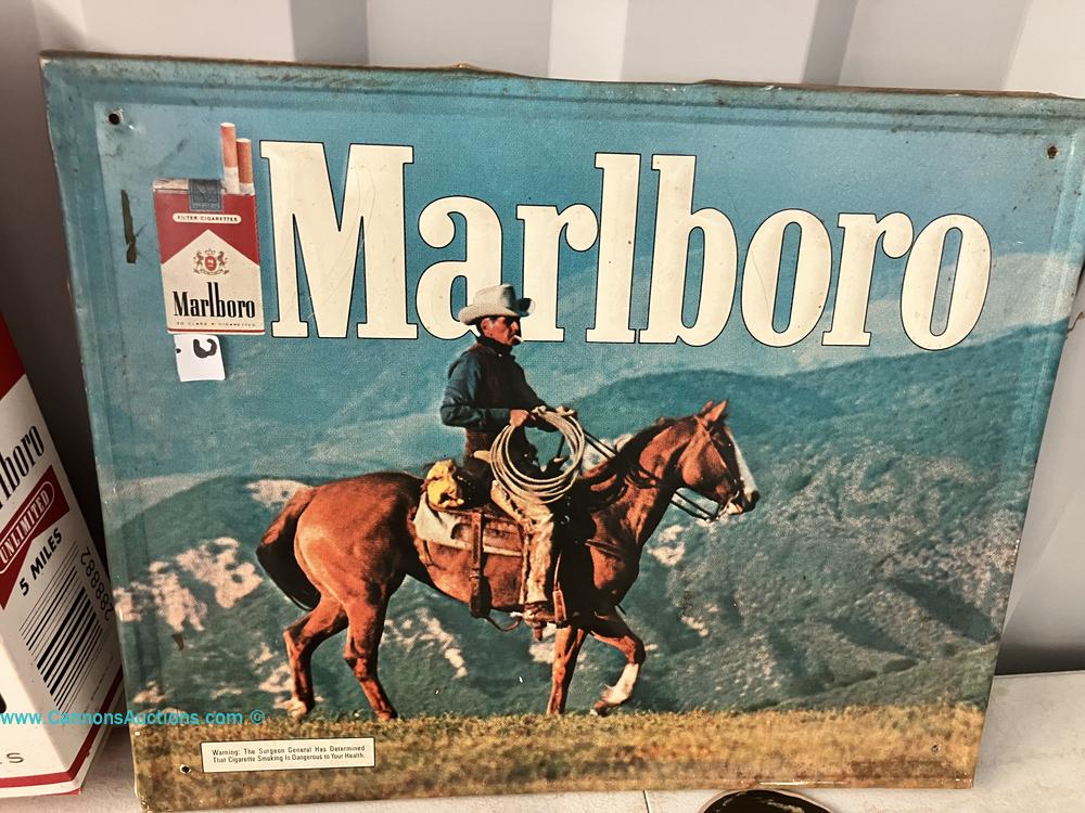Vintage Marlboro metal advertising sign featuring a cowboy on horseback against a mountain landscape.