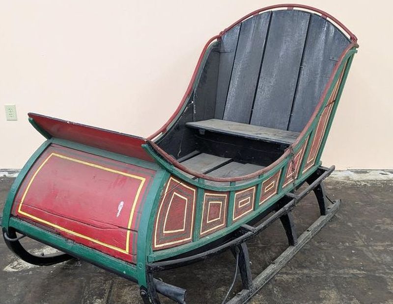 Antique painted wooden horse-drawn sleigh with red, green, and yellow panels and metal runners, measuring 51 x 77 x 39 inches, at Cannon's Auctions in Richmond VA.
